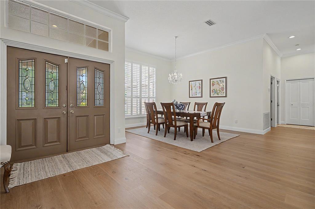 A dining area with a wooden table and chairs sits near a large front entryway — 1319 FORESTEDGE BOULEVARD, OLDSMAR, FL