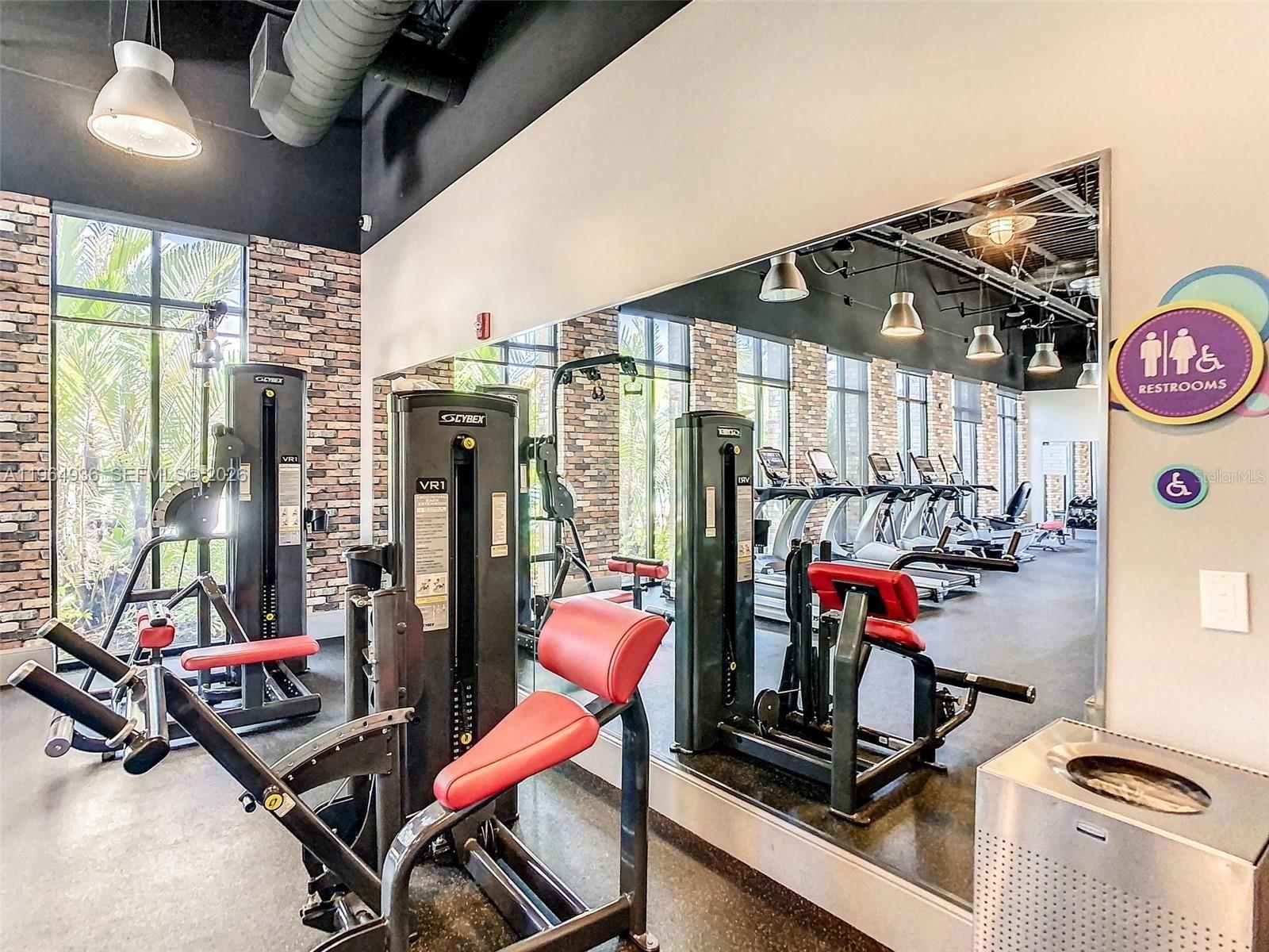 A gym room features brick walls, exercise machines, a large mirror, and industrial ceiling lights — 742 Langboat Dr, Davenport FL 33896, DAVENPORT, FL