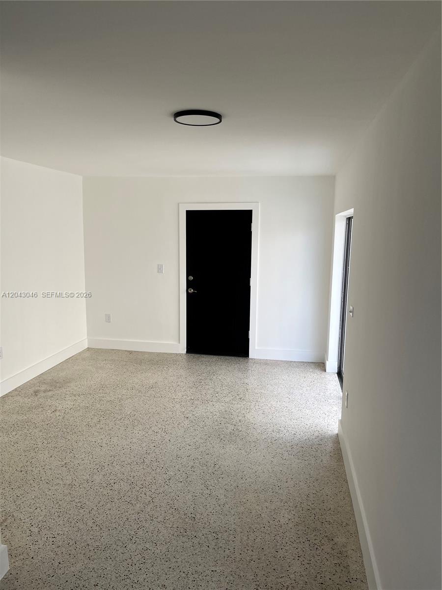 An empty room features white walls, a black door, and speckled flooring — 2010 SW 6th St # 4, Miami FL 33135, MIAMI, FL