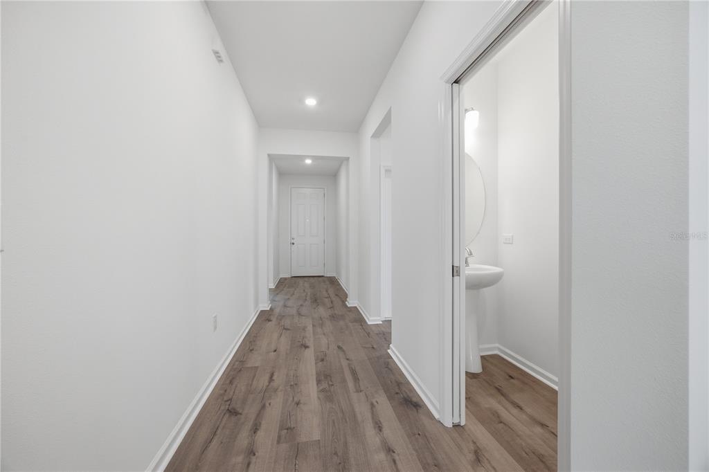 A hallway with wood-look flooring leads to a closed door and a small powder room — 5715 HIAWASSEE ROAD, OKAHUMPKA, FL
