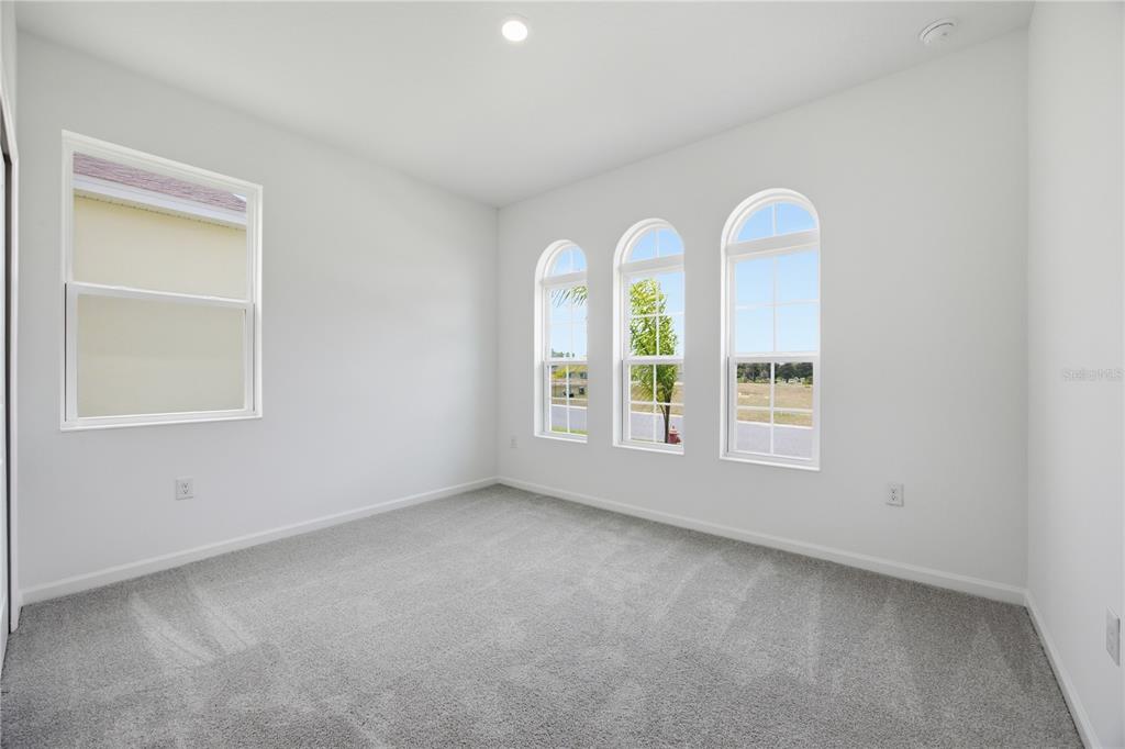 An empty bedroom with gray carpet, white walls, and three arched windows overlooking a field — 5715 HIAWASSEE ROAD, OKAHUMPKA, FL