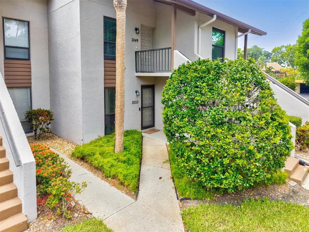 A two-story apartment building exterior features a ground-level entrance, an upper balcony, and landscaping — 3053 TAYWOOD MEADOWS UNIT 3, SARASOTA, FL