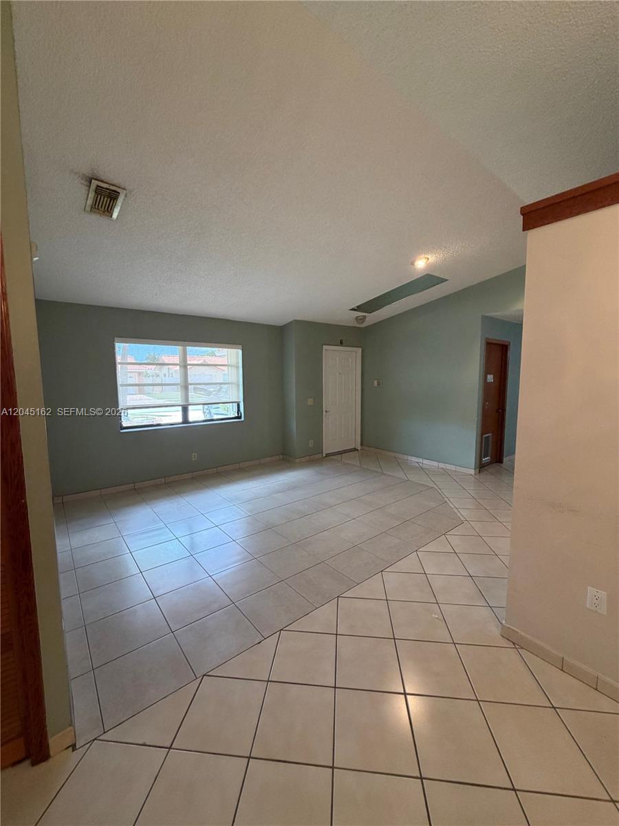 An empty room features light-colored tile flooring, a white door, and a large window — 3262 SW 139th Pl, Miami FL 33175, MIAMI, FL