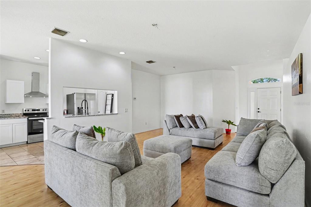 A living room with light wood floors and gray furniture opens to a white kitchen — 3614 TRAPNELL RIDGE DR, PLANT CITY, FL