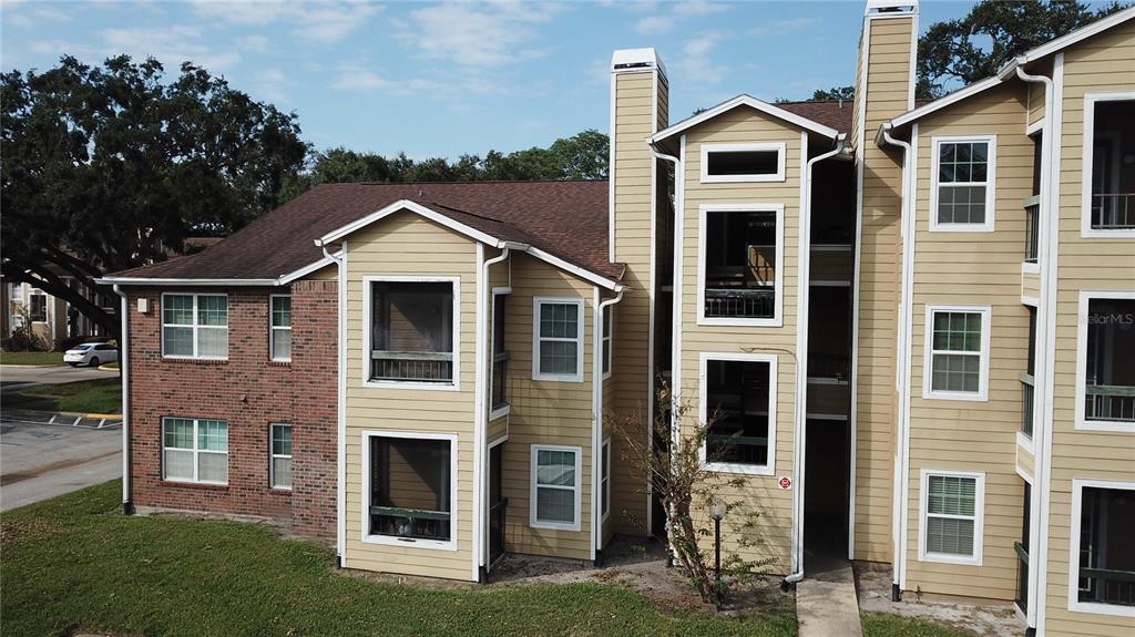 An exterior view of a multi-story apartment building with tan siding and brick accents — 5600 DEVONBRIAR WAY UNIT N202, ORLANDO, FL
