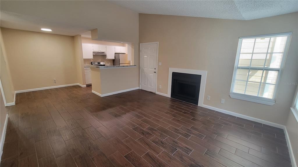 A living room with wood-look tile flooring, a fireplace, and an adjacent kitchen — 5600 DEVONBRIAR WAY UNIT N202, ORLANDO, FL