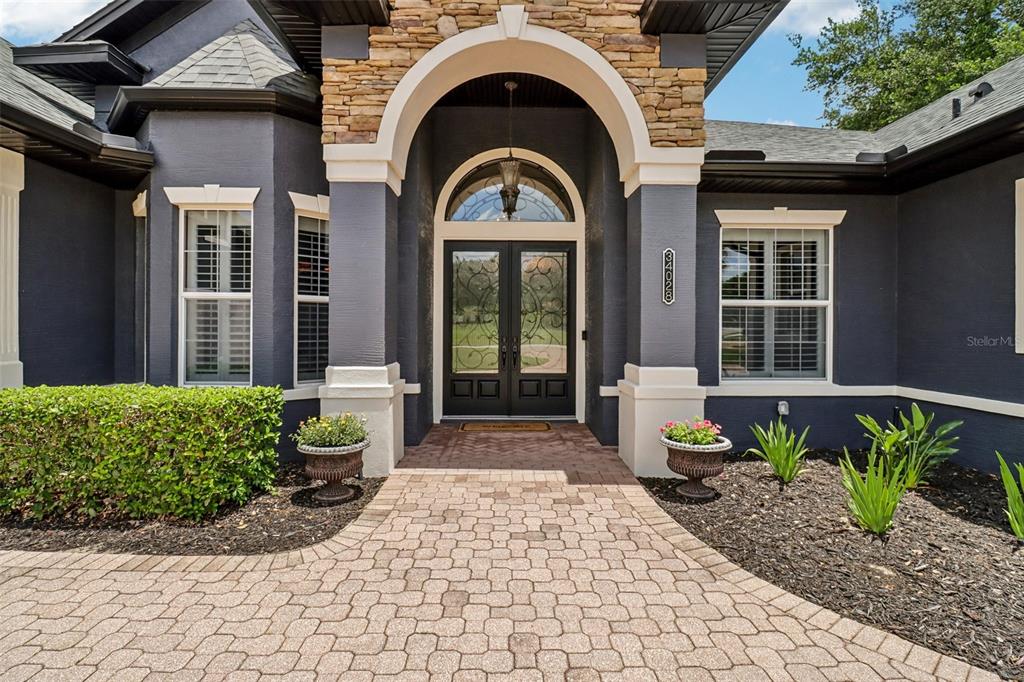 The exterior of a dark-painted house features a stone-accented arched entryway and brick walkway — 34028 MATTHEWS COVE, LEESBURG, FL