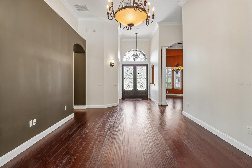 A spacious foyer features dark hardwood floors, a large chandelier, and double front entry doors — 34028 MATTHEWS COVE, LEESBURG, FL