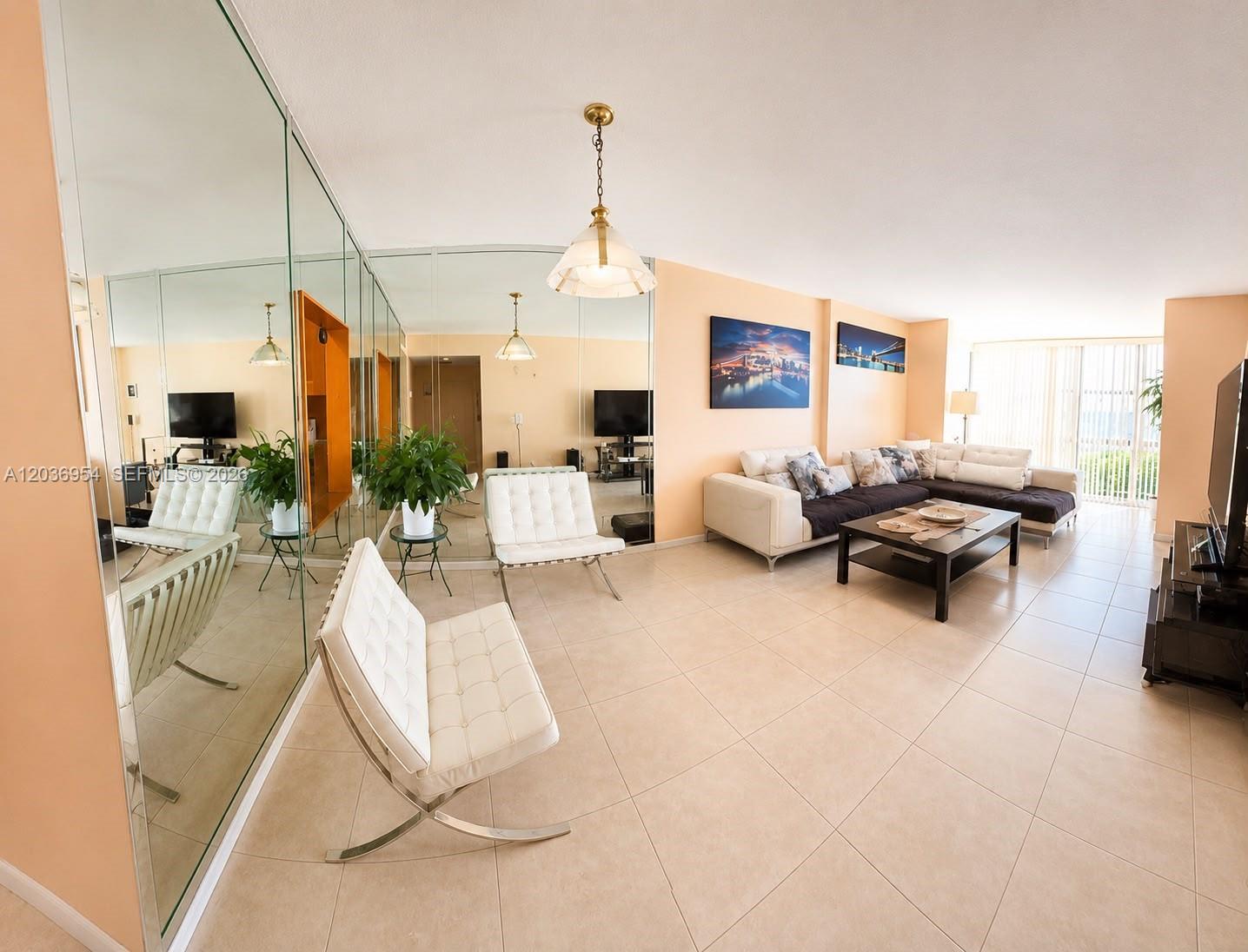 A living room features tiled floors, mirrored walls, white leather chairs, and a sectional sofa — 1000 Parkview Dr # 505, Hallandale Beach FL 33009, HALLANDALE BEACH, FL