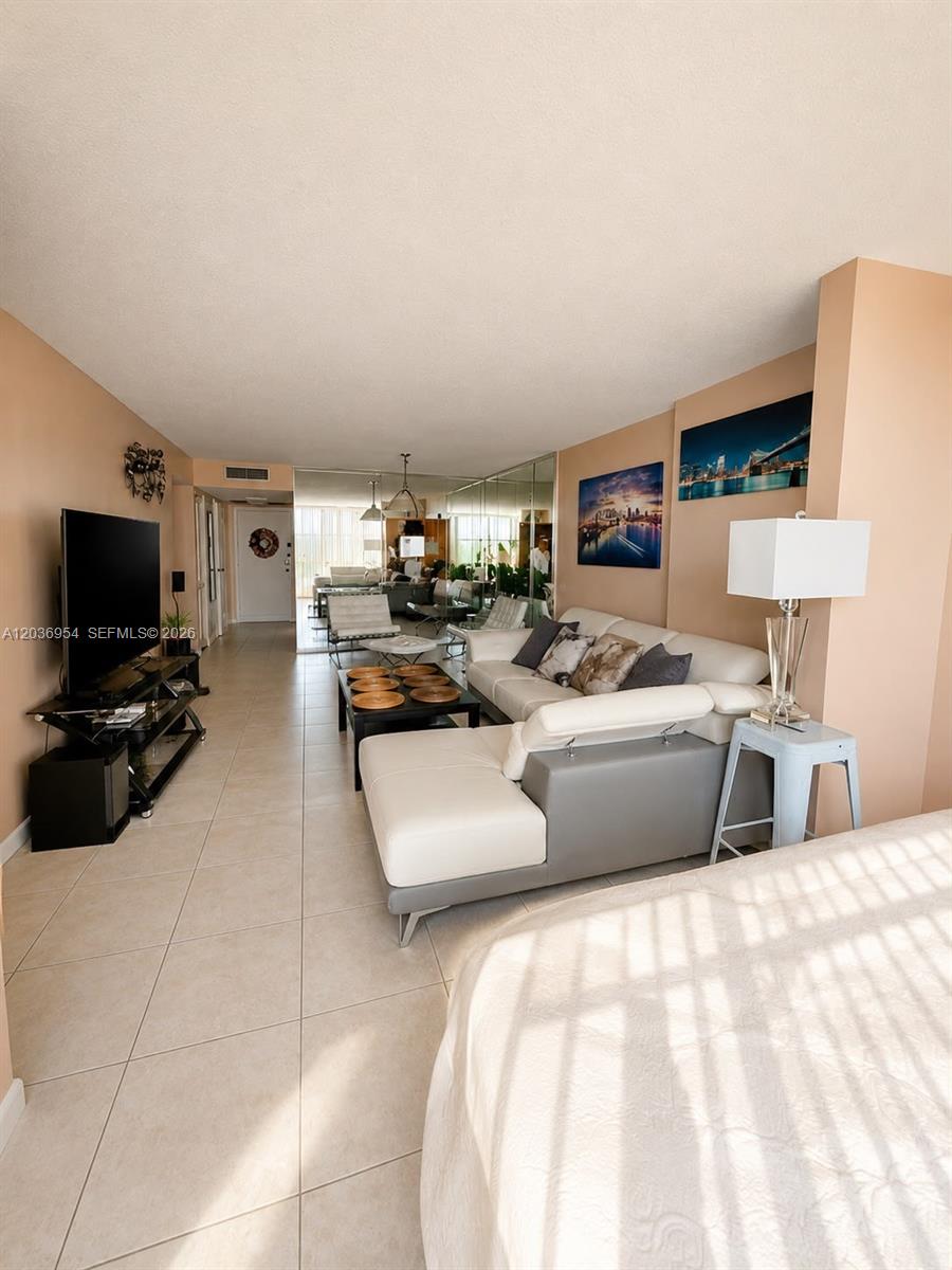 A living room features a white sectional sofa, a television on a stand, and tiled floors — 1000 Parkview Dr # 505, Hallandale Beach FL 33009, HALLANDALE BEACH, FL