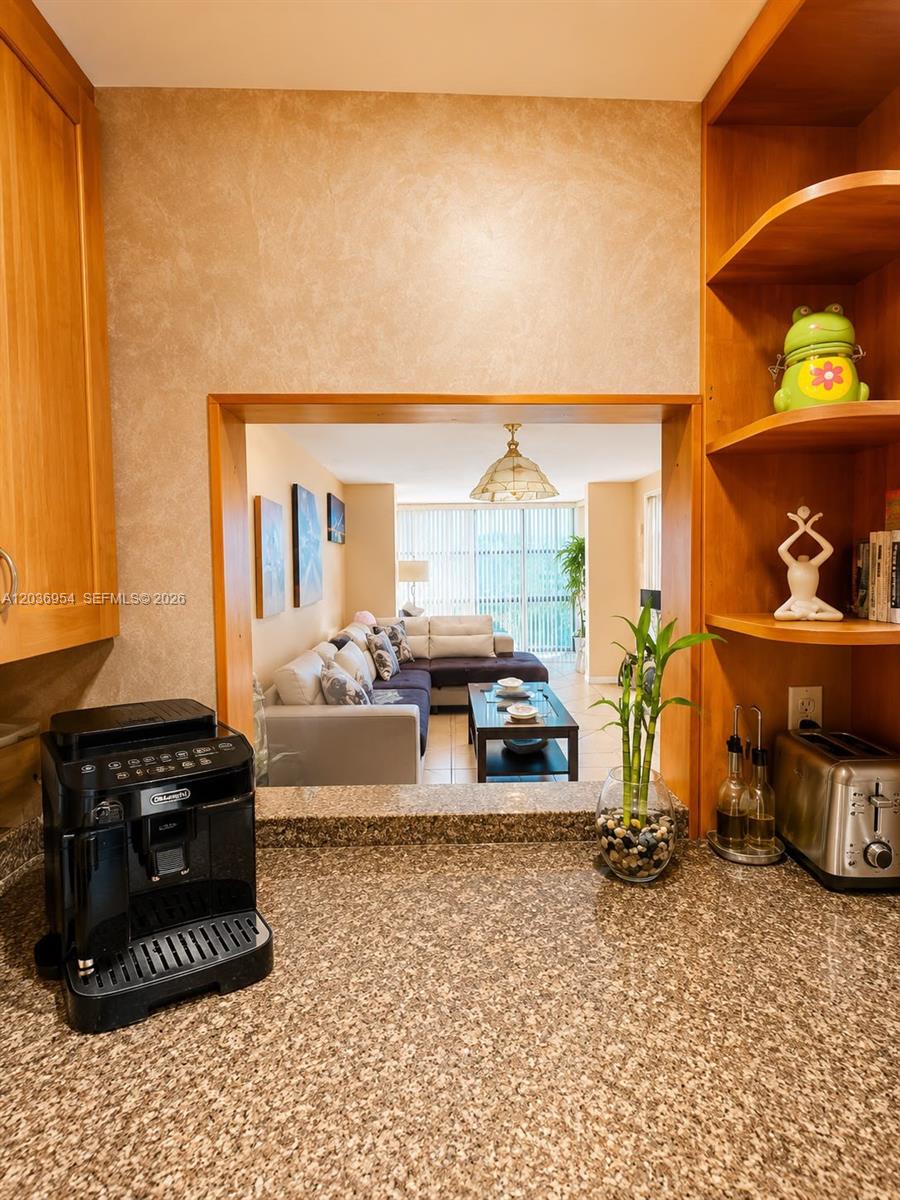 A kitchen counter with a coffee machine overlooks a living room with a sectional sofa — 1000 Parkview Dr # 505, Hallandale Beach FL 33009, HALLANDALE BEACH, FL