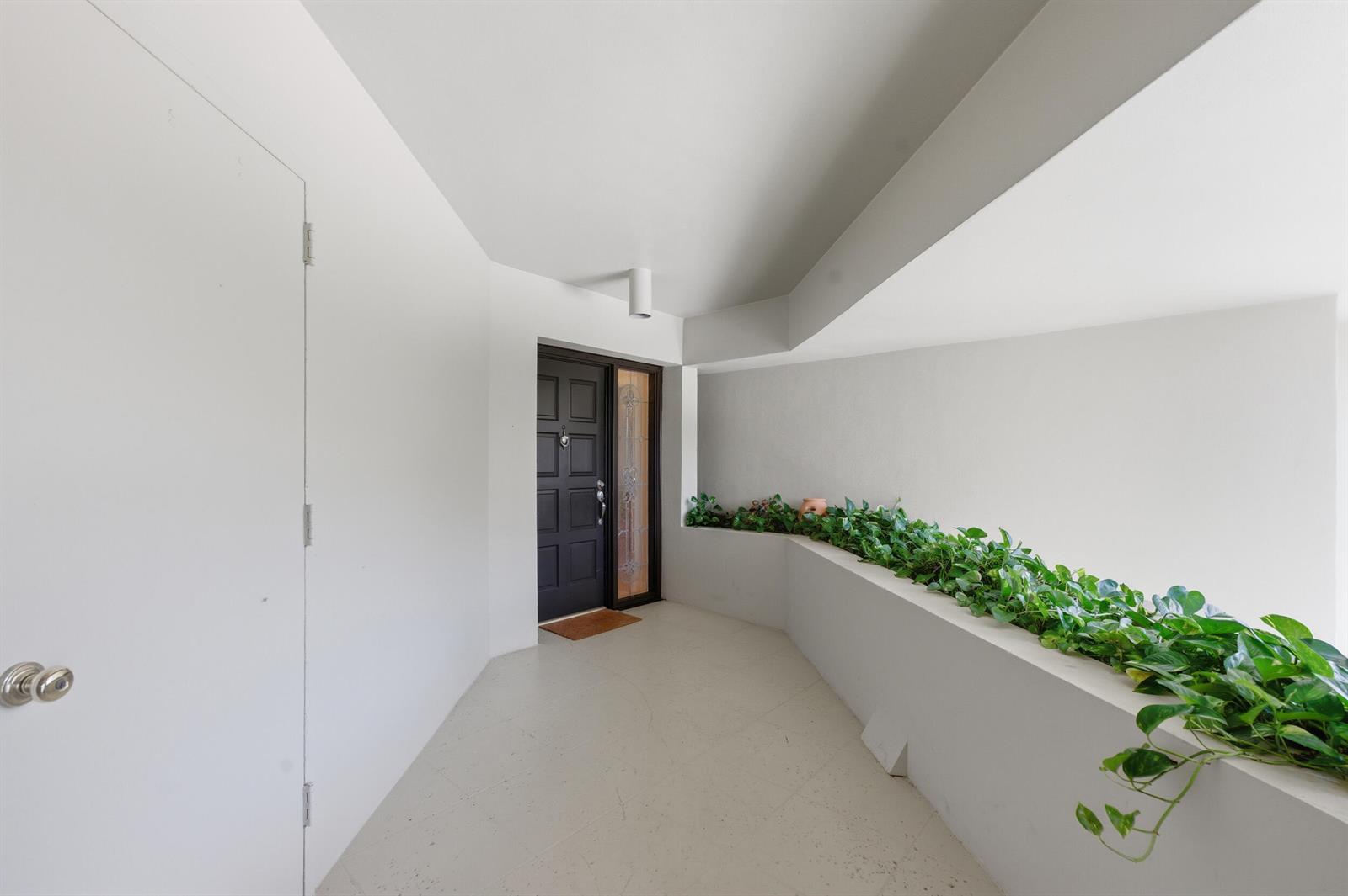 A white entryway features a dark front door and a built-in planter with green vines — 1109 E Marine Way E, North Palm Beach FL 33408, NORTH PALM BEACH, FL