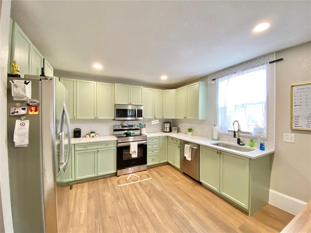 A kitchen features light green cabinets, stainless steel appliances, white countertops, and wood-look flooring — 908 E 20TH AVENUE, TAMPA, FL