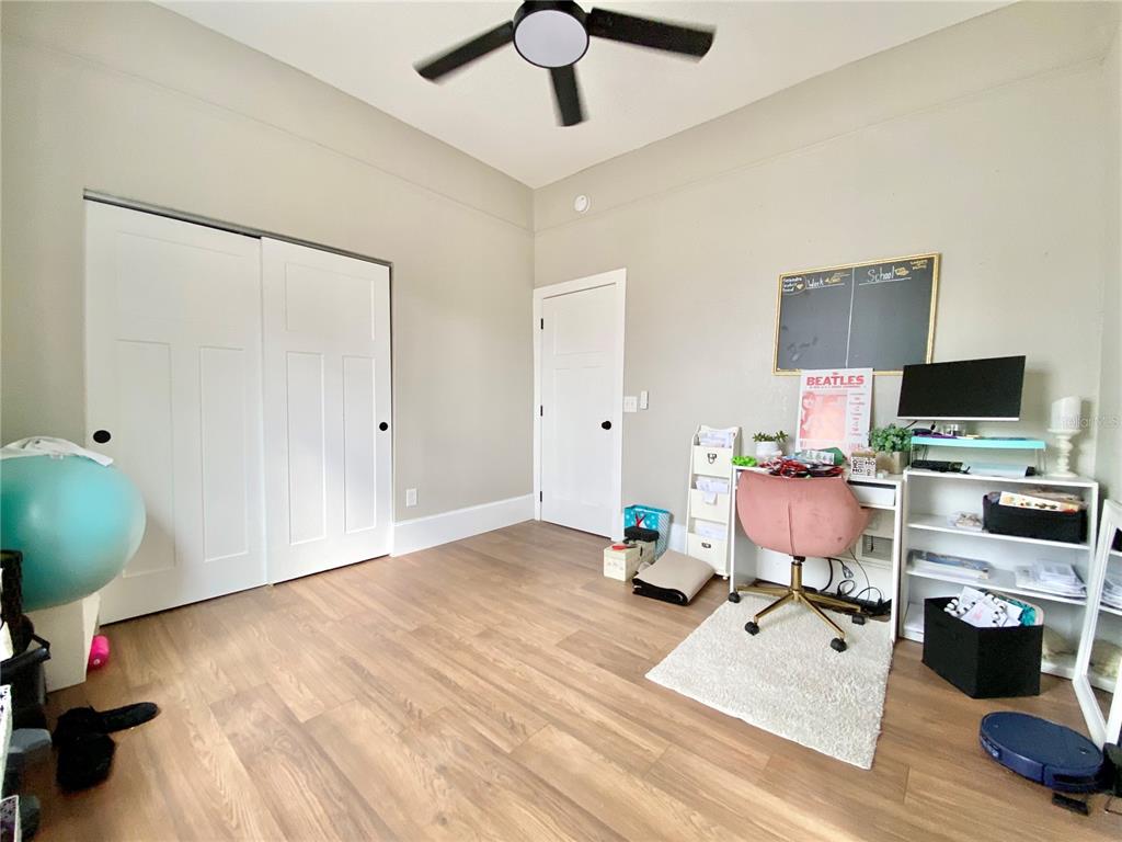 A bedroom features light-colored walls, wood-look flooring, a ceiling fan, and a desk area — 908 E 20TH AVENUE, TAMPA, FL