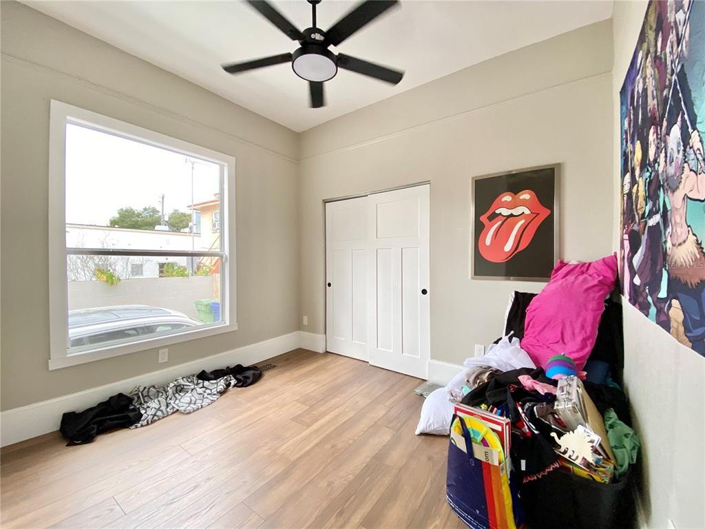A bedroom features light-colored walls, wood-look flooring, a ceiling fan, and a sliding closet door — 908 E 20TH AVENUE, TAMPA, FL