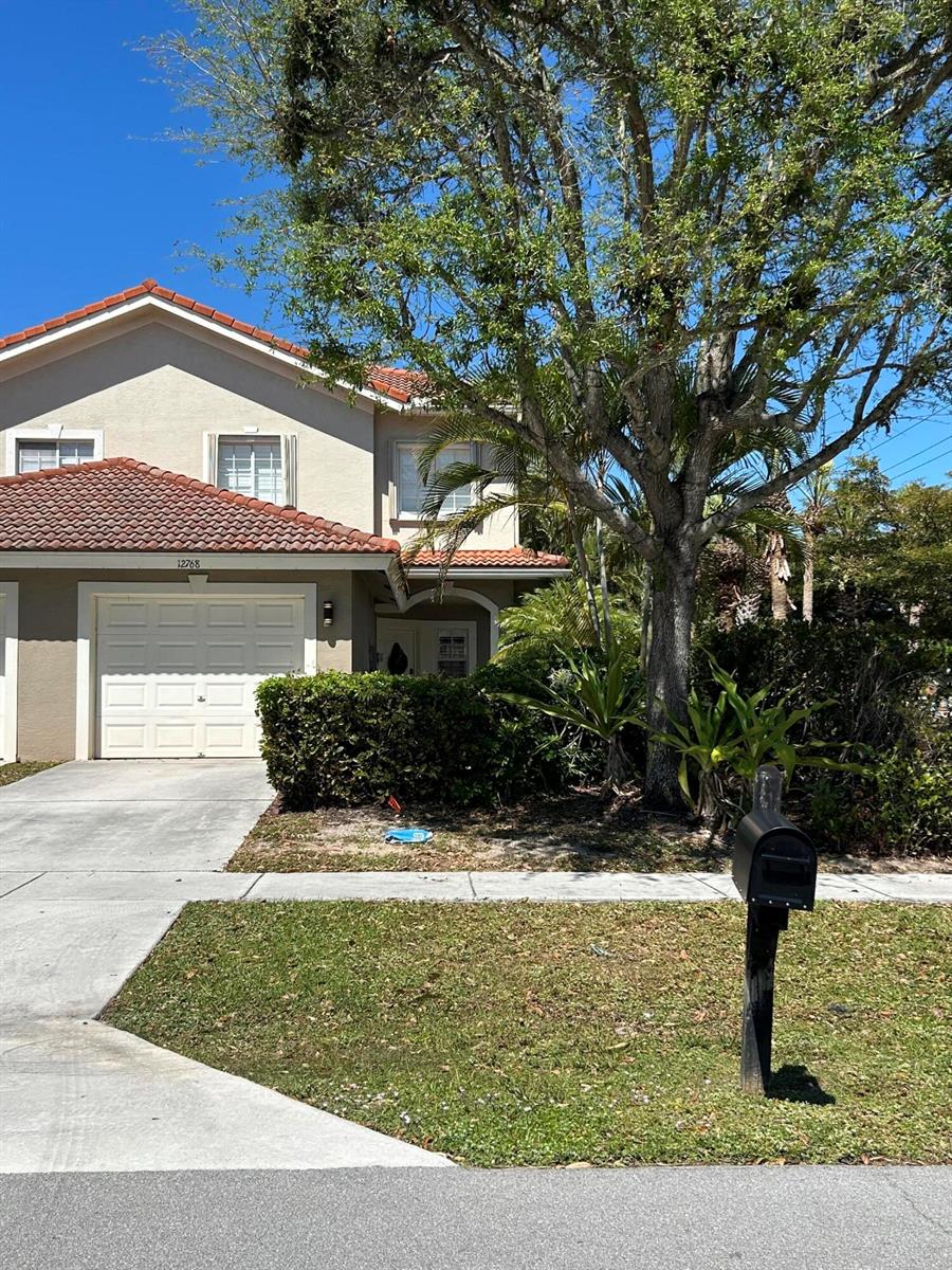 A two-story townhouse with a tile roof, garage, and a large tree in the front — 12768 Westhampton Circle, Wellington FL 33414, WELLINGTON, FL