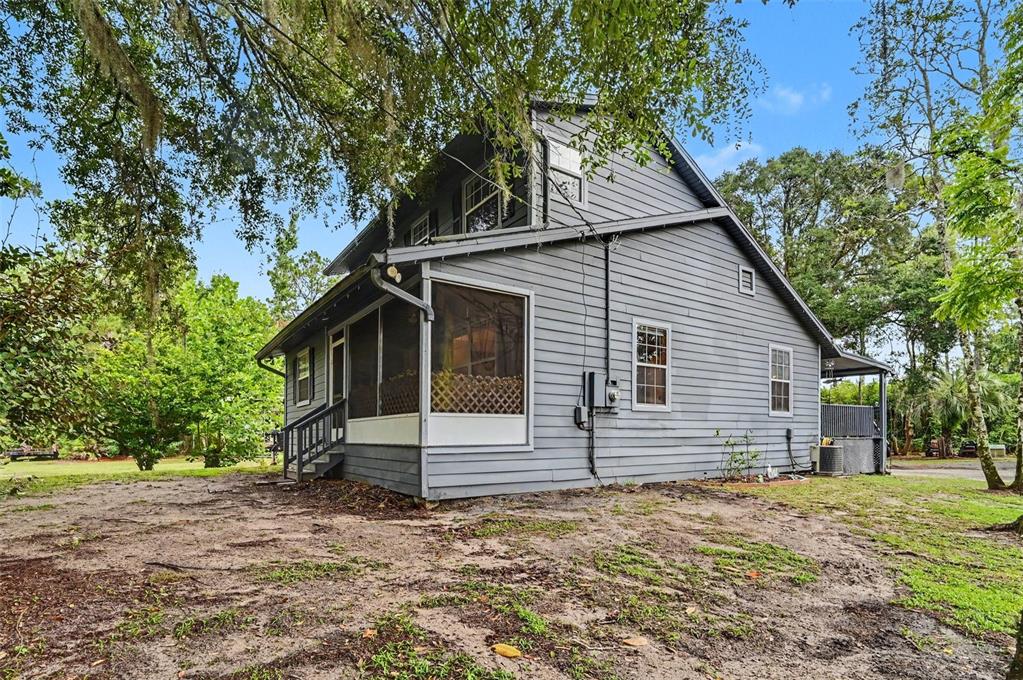 A gray two-story house with a screened-in porch stands on a dirt lot with trees — 490 PINE WOODS ROAD, ORMOND BEACH, FL