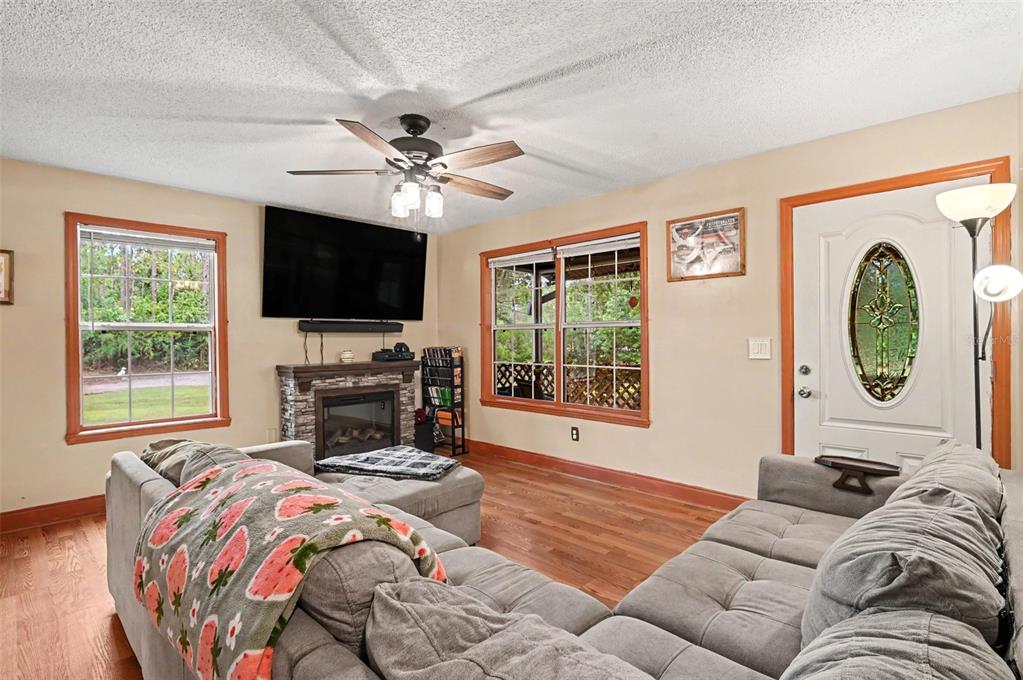 A living room features a gray sectional sofa, a stone fireplace with a television, and hardwood floors — 490 PINE WOODS ROAD, ORMOND BEACH, FL
