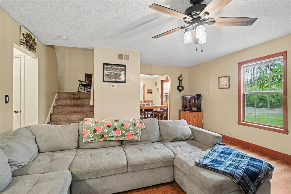 A living room features a gray sectional sofa, a ceiling fan, and carpeted stairs — 490 PINE WOODS ROAD, ORMOND BEACH, FL