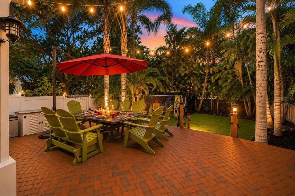 A brick patio features a dining set under a red umbrella with string lights above — 2869 BAYSHORE TRAILS DRIVE, TAMPA, FL