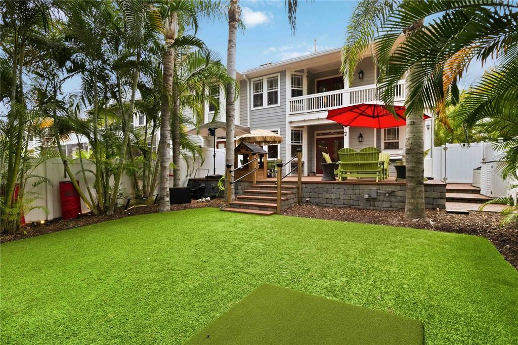 A backyard features a raised wooden deck with a red umbrella and artificial grass lawn — 2869 BAYSHORE TRAILS DRIVE, TAMPA, FL