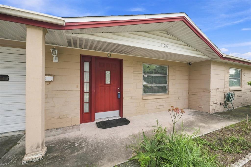 The exterior of a beige house features a red front door and a concrete porch — 4126 WIGGINS DRIVE, NEW PORT RICHEY, FL
