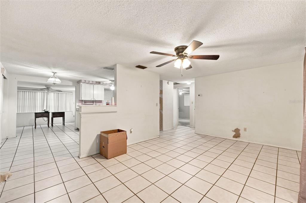 An open-concept living and dining area features white tile flooring, a ceiling fan, and walls — 4126 WIGGINS DRIVE, NEW PORT RICHEY, FL