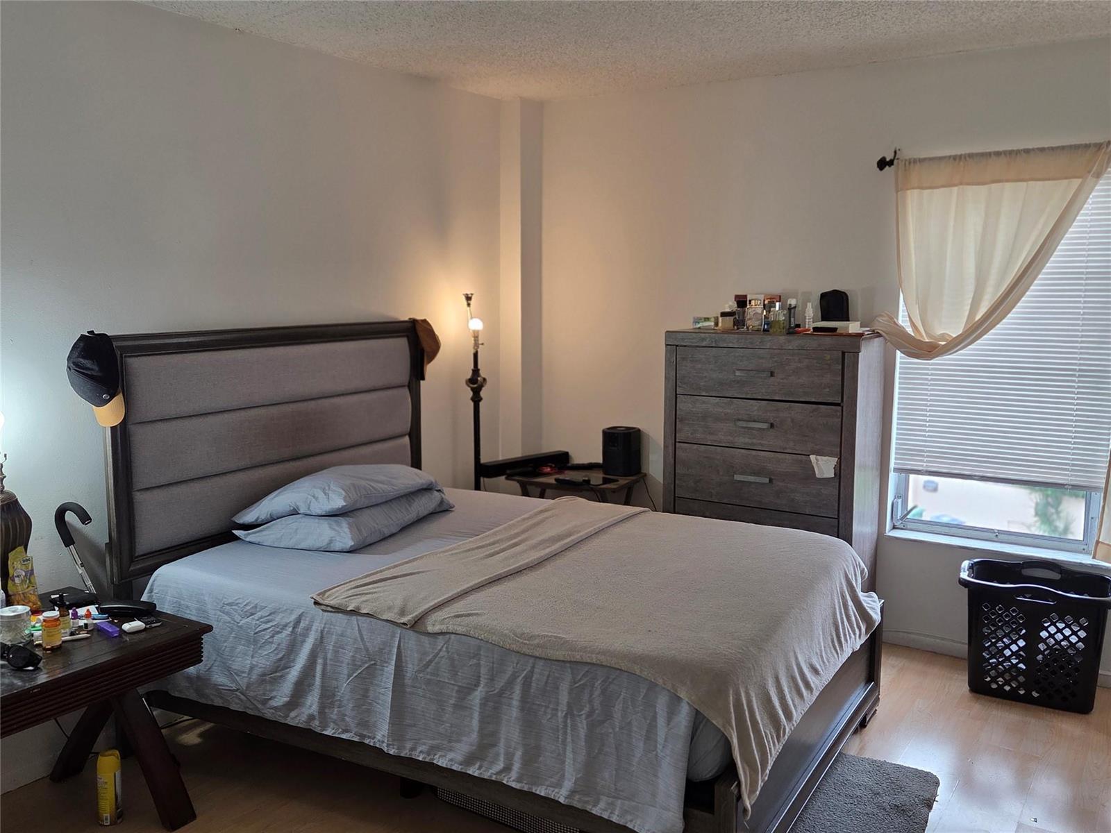 A bedroom featuring a gray upholstered bed, a matching dresser, and a window with blinds — 4152 Inverrary Drive # 310, Lauderhill FL 33319, LAUDERHILL, FL