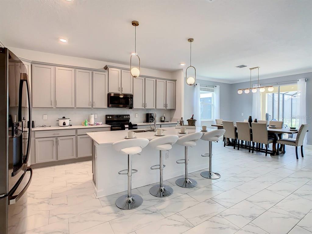 A modern kitchen features light gray cabinets, a white quartz island with barstools, and marble-look flooring — 2908 PROTAGONIST STREET, KISSIMMEE, FL