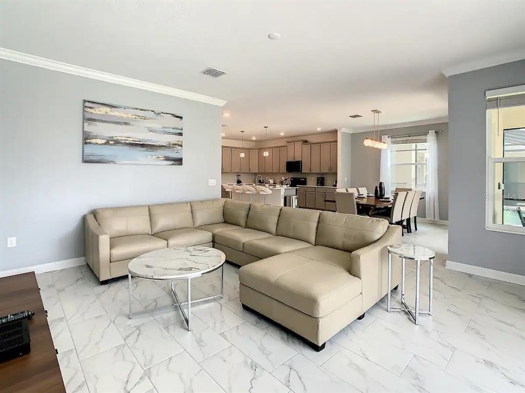 A living room with a large beige sectional sofa and marble-look tile floors opens to a kitchen — 2908 PROTAGONIST STREET, KISSIMMEE, FL