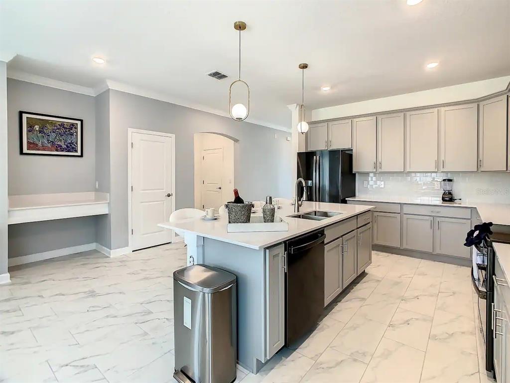 A modern kitchen features gray cabinets, a white island with a sink, and marble-look flooring — 2908 PROTAGONIST STREET, KISSIMMEE, FL