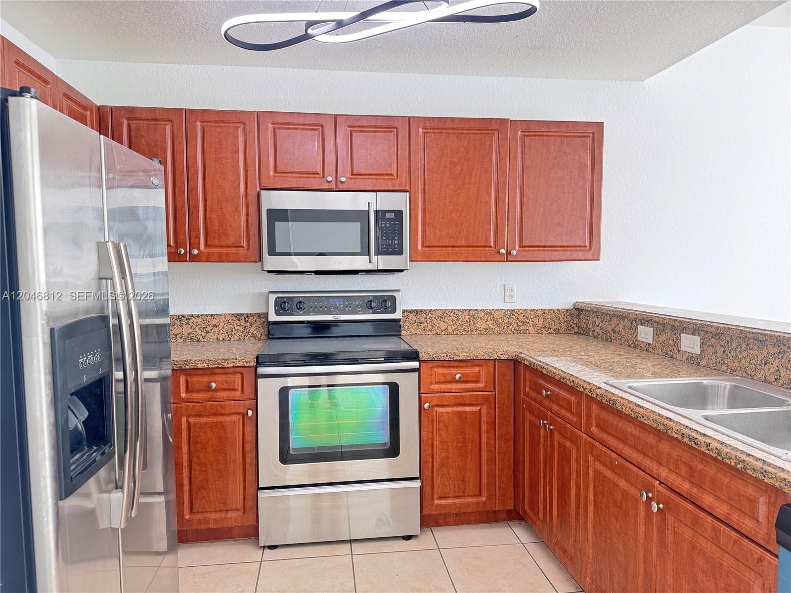 A kitchen features wood cabinets, granite countertops, stainless steel appliances, and tile flooring — 11102 NW 83rd St # 203, Doral FL 33178, DORAL, FL