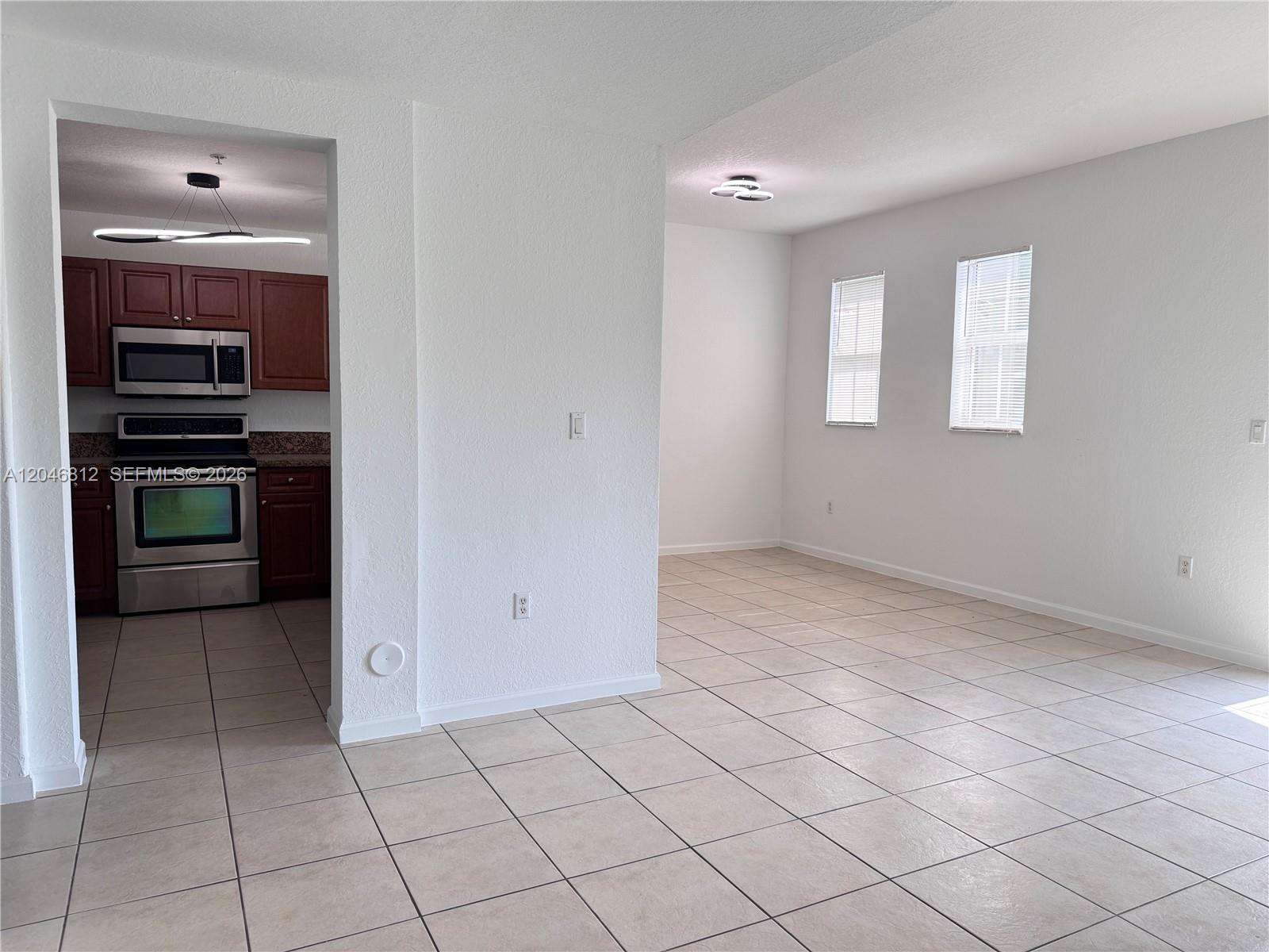 A kitchen with dark wood cabinets and stainless appliances sits adjacent to a tiled room — 11102 NW 83rd St # 203, Doral FL 33178, DORAL, FL