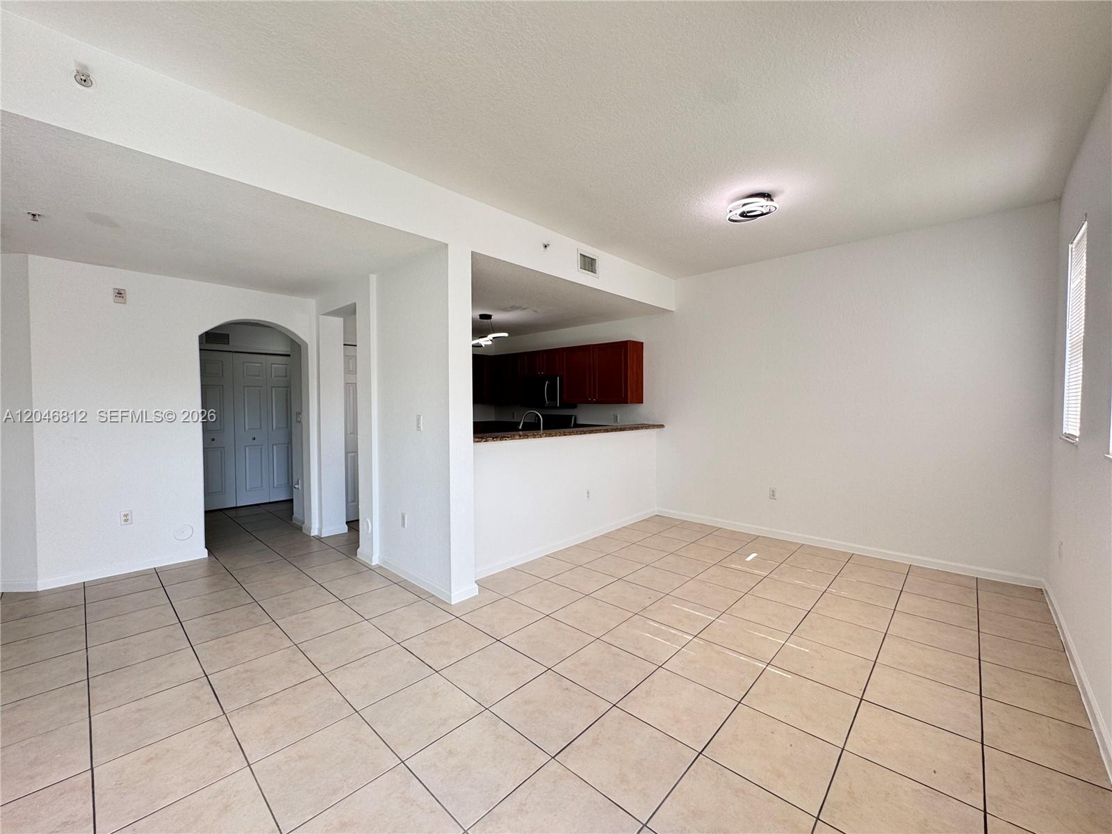 An open-concept living area features beige tile flooring, white walls, and a kitchen pass-through — 11102 NW 83rd St # 203, Doral FL 33178, DORAL, FL