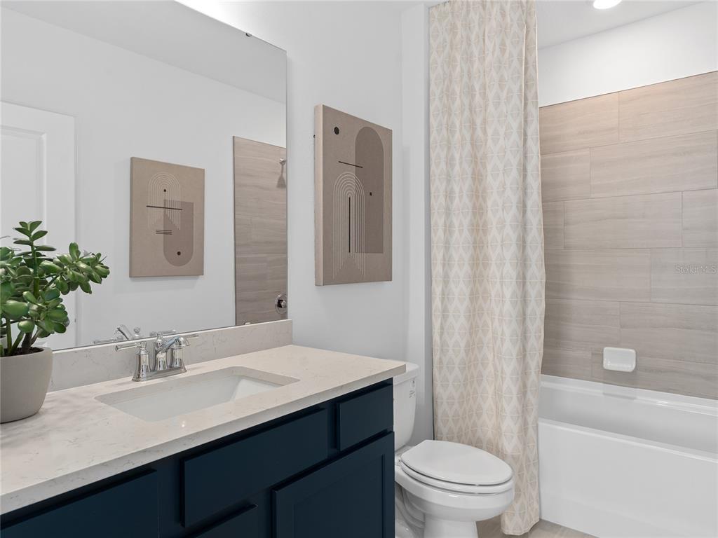 A bathroom features a dark blue vanity, a light countertop, and a tiled tub shower — 5690 ENCHANTED MEADOW ALLEY, CLERMONT, FL
