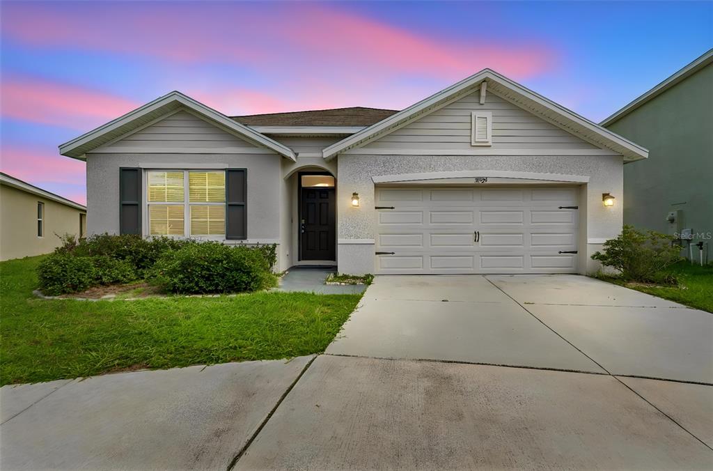 A single-story house with a light-colored stucco exterior, a two-car garage, and a front lawn — 35525 STELLA VAST DRIVE, ZEPHYRHILLS, FL