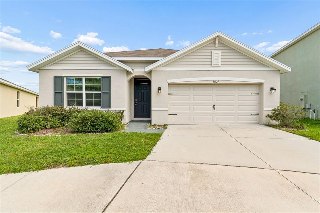 A single-story house with beige siding, a two-car garage, and a dark front door — 35525 STELLA VAST DRIVE, ZEPHYRHILLS, FL