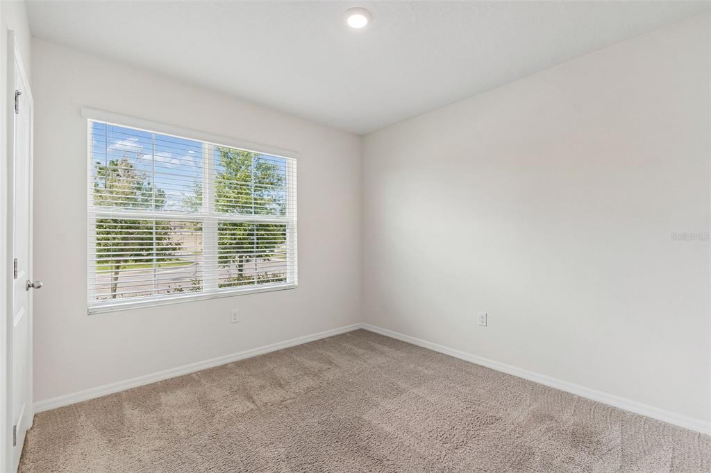 An empty bedroom features beige carpet, white walls, and a window with white blinds — 35525 STELLA VAST DRIVE, ZEPHYRHILLS, FL