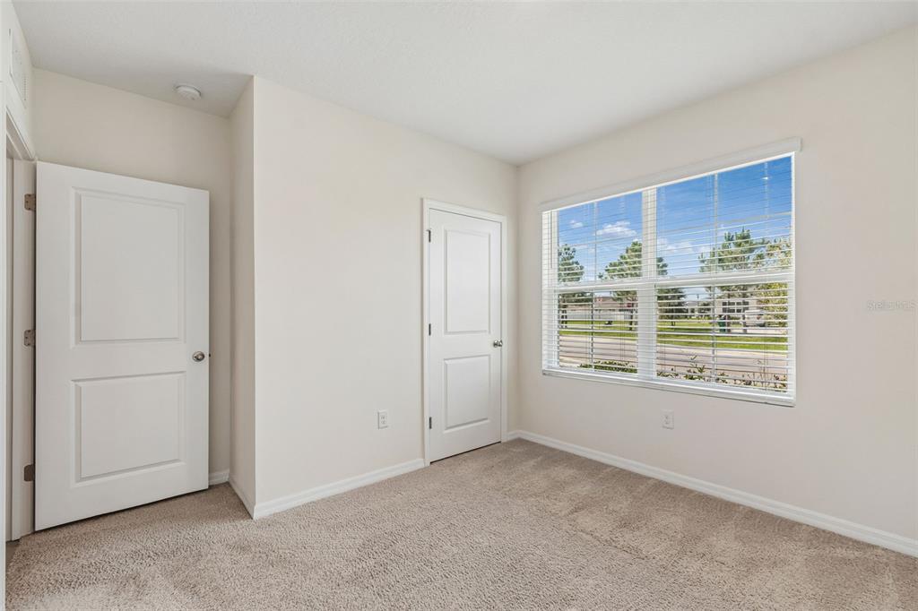 An empty bedroom features beige carpet, white walls, two closed doors, and a large window — 35525 STELLA VAST DRIVE, ZEPHYRHILLS, FL