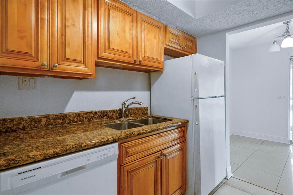 A kitchen features wood cabinets, granite countertops, a double sink, and white appliances — 4709 S TEXAS AVENUE UNIT 4709D, ORLANDO, FL