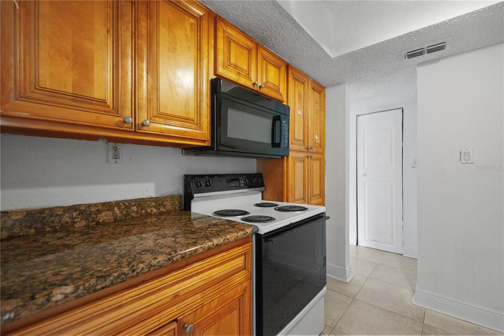 A kitchen features wood cabinets, a black microwave, a white stove, and granite countertops — 4709 S TEXAS AVENUE UNIT 4709D, ORLANDO, FL