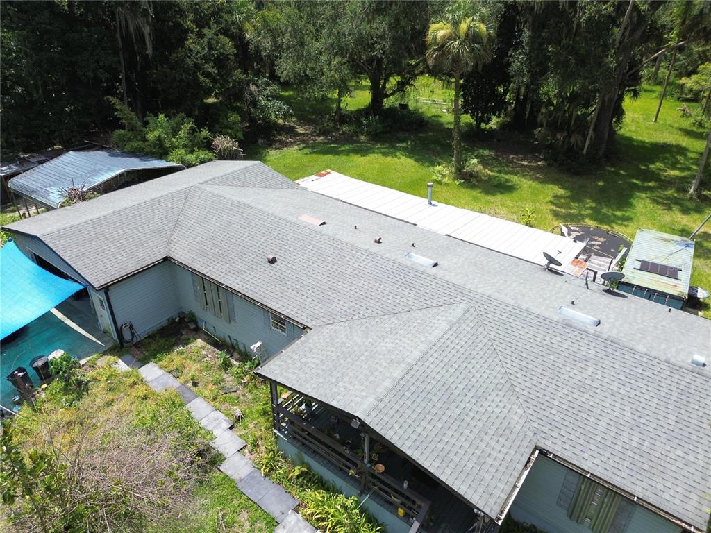 An aerial view shows the shingled roof of a house with an attached metal-roofed section — 335 STACY GROVE RD , ROAD, OAK HILL, FL