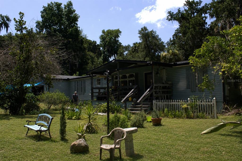 A light-colored mobile home with a front porch sits in a grassy, tree-filled yard — 335 STACY GROVE RD , ROAD, OAK HILL, FL
