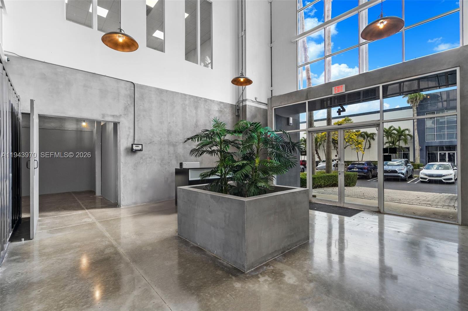 A modern industrial-style lobby features concrete floors, a large central planter, and floor-to-ceiling windows — 7620 NW 25th St # 4, Miami FL 33122, MIAMI, FL