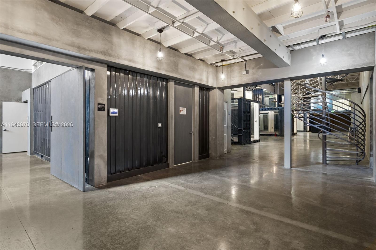 An industrial-style interior features concrete floors, exposed ceiling beams, and a metal spiral staircase — 7620 NW 25th St # 4, Miami FL 33122, MIAMI, FL