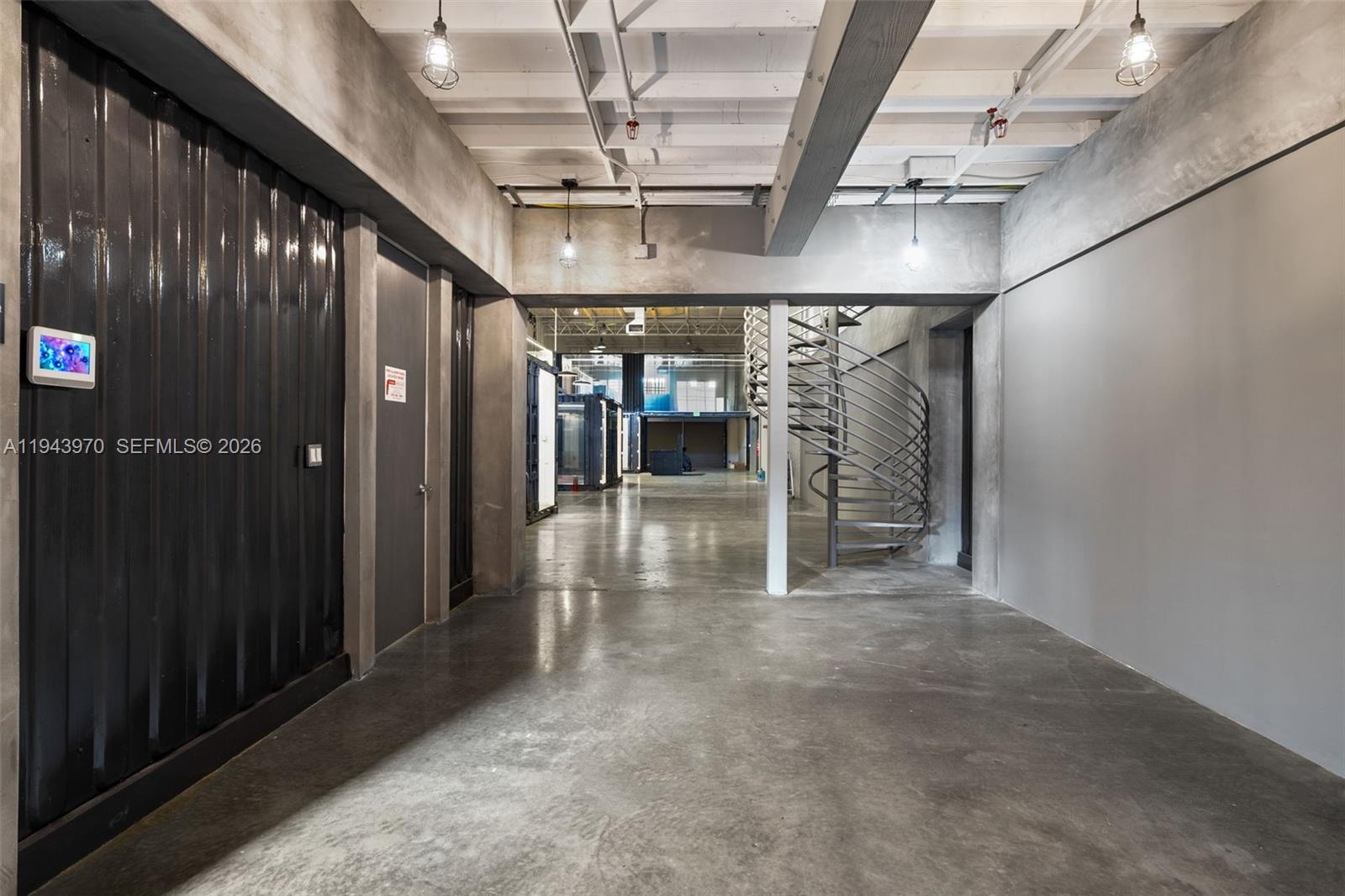 An industrial-style interior features a concrete floor, exposed ceiling beams, and a spiral staircase — 7620 NW 25th St # 4, Miami FL 33122, MIAMI, FL