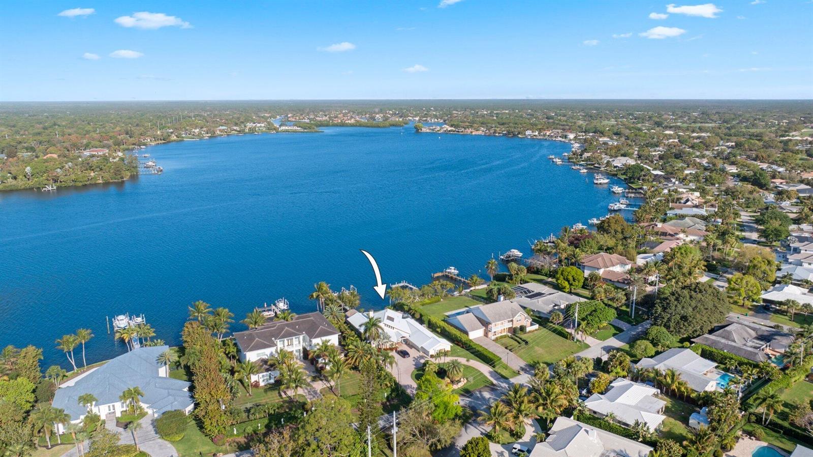 An aerial view shows a waterfront house with a dock on a large lake — 163 River Drive, Tequesta FL 33469, TEQUESTA, FL