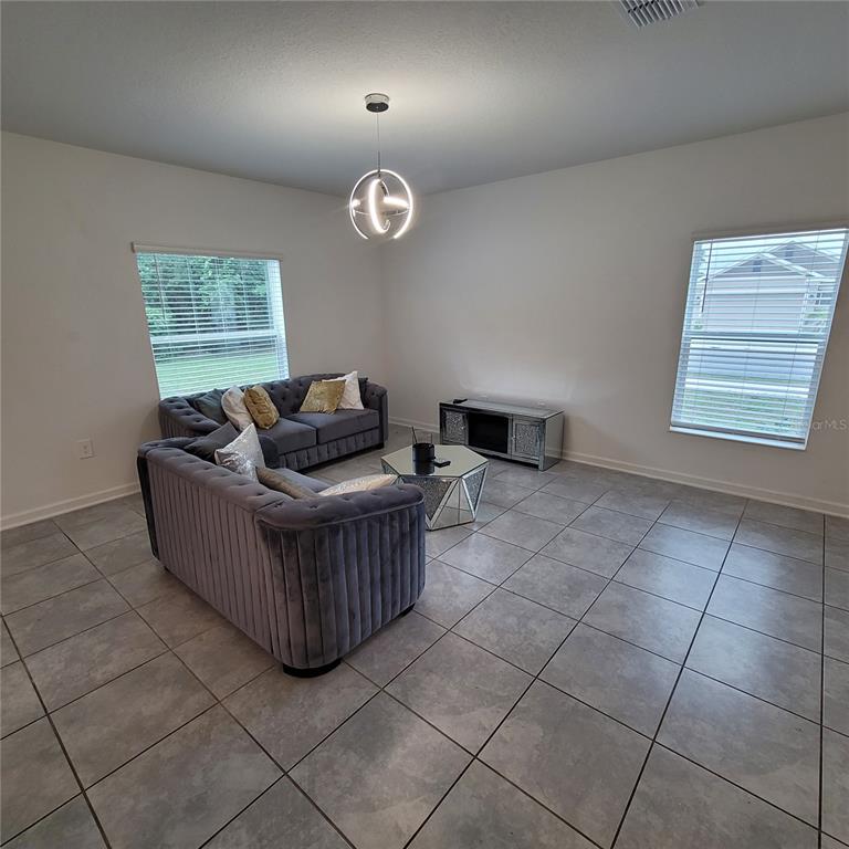 A living room features gray tile flooring, two tufted sofas, a mirrored coffee table, and windows — 577 BELL PRAIRIE CIRCLE, LAKE WALES, FL