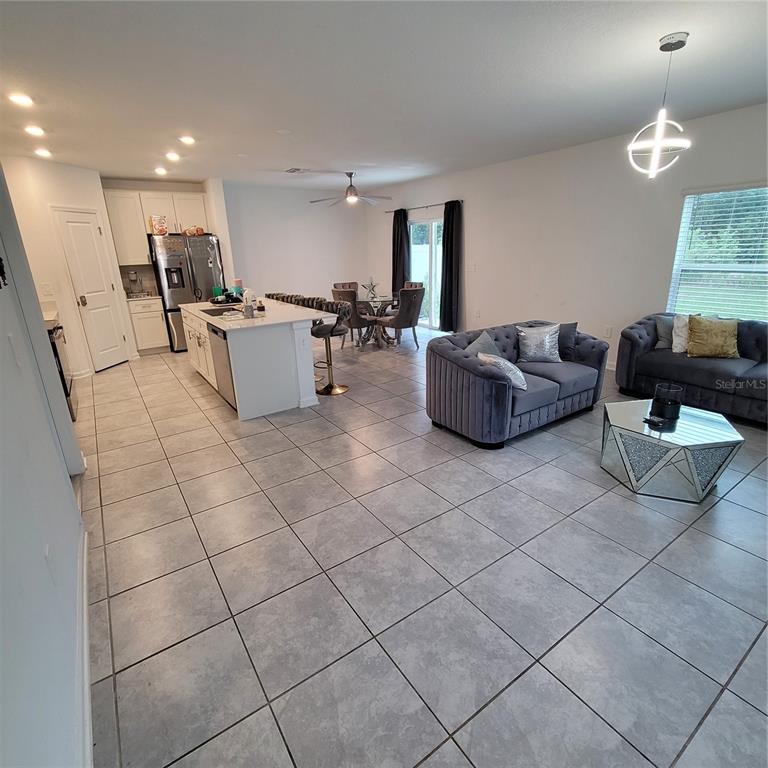 An open-concept living room and kitchen featuring tile flooring, white cabinetry, and gray furniture — 577 BELL PRAIRIE CIRCLE, LAKE WALES, FL