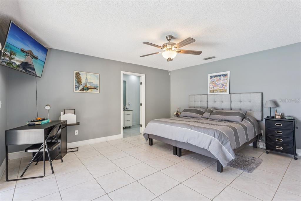 A bedroom features a bed with a gray headboard, a desk, and tile flooring — 8215 ROLLA COURT, ORLANDO, FL